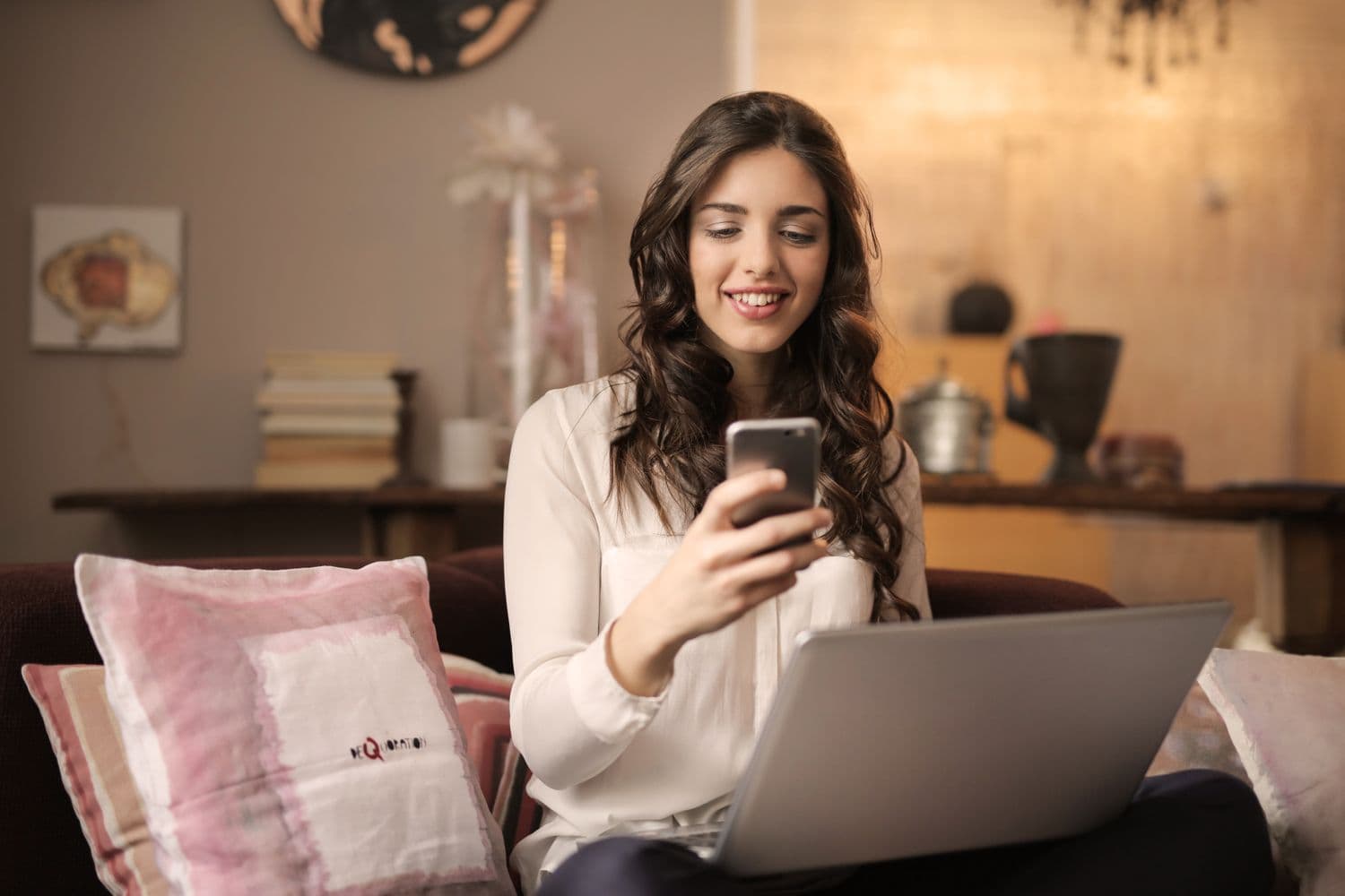 Jovem brasileira sorrindo com o celular, em casa